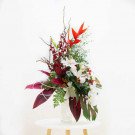 Tropical floral arrangement with lilies, orchids, heliconia, and foliage in a vase.