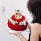 Round red flower cake with Ferrero Rocher chocolates and a "Happy Birthday" topper, held by a woman.