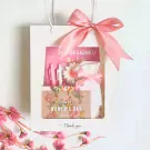 Pink gift bag with a ribbon bow, featuring pens, a notebook, a flower, and a Women's Day card.