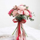 Bridal bouquet of pink roses, gerbera daisies, and carnations with eucalyptus, tied with a red and pink ribbon.