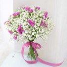 A bridal bouquet of white baby's breath and purple flowers tied with a pink ribbon.