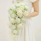 A bride in a white dress holding a cascading bouquet of white roses and baby's breath.
