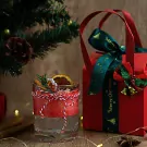 Christmas candle with dried orange, cinnamon, and rosemary in a glass, tied with red and white string, next to a red gift box.