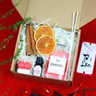 Gift box with red candle, reed diffuser, dried oranges, cinnamon sticks, and a tag.