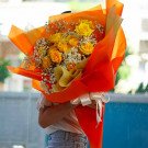 Vibrant yellow roses and baby's breath bouquet wrapped in bright orange and yellow paper, tied with a white ribbon.