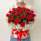 A round pink box filled with red roses and baby's breath, tied with a red ribbon.