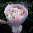 A bouquet of light pink and white roses, carnations, and gerbera daisies wrapped in pink and white paper with a straw tie.