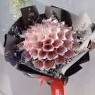 A money bouquet with rolled pink banknotes, black and grey paper, and dried baby's breath.