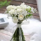 White roses and baby's breath bouquet with lace ribbon, ideal for weddings.