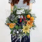 Christmas wreath with pine cones, dried oranges, cinnamon sticks, and "Merry Christmas" sign.