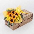 Bright yellow sunflowers and yellow chrysanthemums arranged in a bouquet with eucalyptus in a cardboard box.