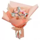 A bouquet of pink and orange roses with green leaves, wrapped in peach paper and tied with a white ribbon.