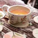 Ceramic teacup with floral designs, filled with layered orange and yellow liquid, on a saucer surrounded by coasters.