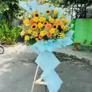 Large bouquet of yellow and orange roses, sunflowers, and hydrangeas on a stand.