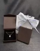 Diamond necklace in an open jewelry box, next to a closed box and a gift bag with a bow.