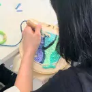 A person is punch needling a colorful abstract design on fabric in a hoop.
