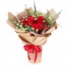 Bouquet of red roses and daisies wrapped in brown paper with a red ribbon.