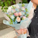 Rainbow dyed roses and blue flowers bouquet with a pink ribbon tied around the stems.
