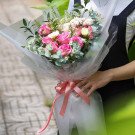 Pink roses and white flowers in a clear bouquet wrap with a pink ribbon.