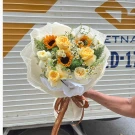 A bouquet of yellow roses, sunflowers, and daisy-like flowers wrapped in sheer paper with a brown ribbon.