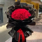 A large bouquet of 150 red roses wrapped in black paper with red ribbon.