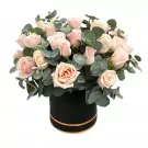 A round black box filled with light pink roses and eucalyptus leaves.