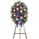 Funeral flower arrangement with red, white, and blue flowers on a wooden easel.