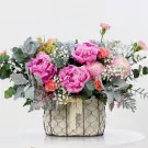 Pink peonies, chrysanthemums, and carnations in a wire basket with lace ribbon.