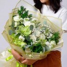 A bouquet of white roses, green anthurium, and various greenery arranged in a yellow wrapper.
