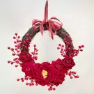 A red rose and berry wreath with a red ribbon bow.