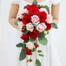 Cascading bouquet of red and pink roses with red berries and greenery.