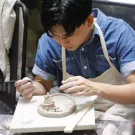 Person sculpting small clay houses with tools in a pottery workshop.