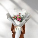 Pink roses, baby's breath, and eucalyptus in a bouquet wrapped in white and grey paper.