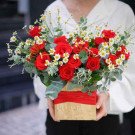 Red roses and white daisies in a wooden box with red ribbon.
