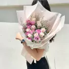 Woman holding a pastel bouquet of pink and white roses with delicate filler flowers.