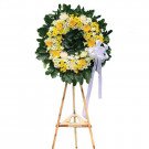 Wreath of yellow and white flowers on a wooden stand with a white ribbon.