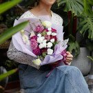 A woman in denim holds a bouquet of purple and white flowers wrapped in light purple paper.