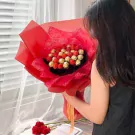 Chocolate and strawberry bouquet with red wrapping and ribbon held by a person.