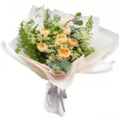 Bouquet of peach roses, white flowers, and greenery wrapped in delicate paper.