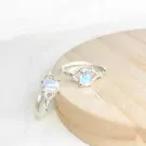 Two silver rings with oval moonstones, one in front and one behind, on a wooden surface.