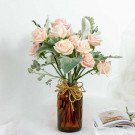 Pink roses and dusty miller in a brown glass vase, tied with twine.