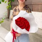 Woman holding a bouquet of 66 red roses wrapped in white paper.