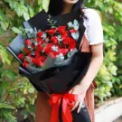 Woman holding a bouquet of 36 red roses wrapped in black paper and tied with a red ribbon.