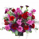A vibrant floral arrangement of red and pink roses, purple carnations, and other greenery in a black box.
