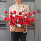 Man holding a basket of red roses, eucalyptus, and red berries.
