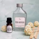 Reed diffuser set with essential oil, reeds, and decorative rattan balls on a marbled surface.
