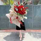 Large bouquet of 150 red roses, elegantly wrapped in beige paper with red ribbons.