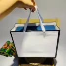 White gift bag with white handles, a blue item inside, and decorative items on the side.