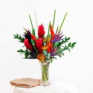 Tropical flower arrangement with red ginger, bird of paradise, and chrysanthemums in a glass vase.