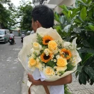 Man holding a bouquet of sunflowers, yellow roses, and daisy-like flowers.